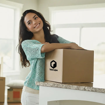 Mujer sonriendo apoyada sobre una caja de cartón TeleCajas, ideal para mudanzas, almacenaje o envíos ecommerce.